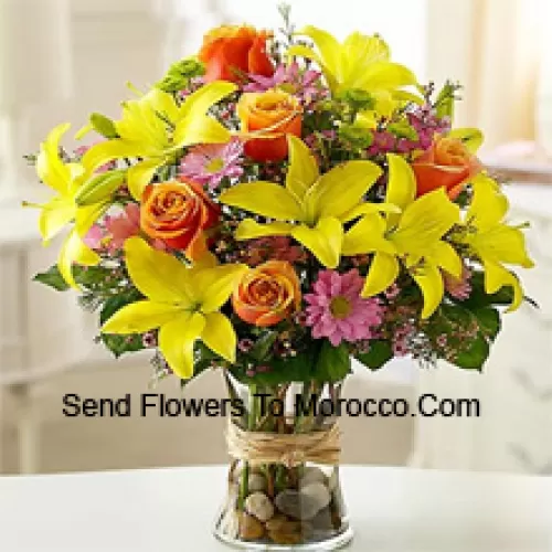 Lys jaunes, roses oranges et gerberas roses avec des remplisseurs saisonniers dans un vase en verre