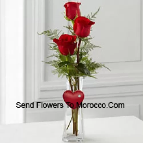 3 Red Roses In A Glass Vase Having A Small Heart Attached To It